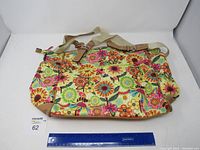 Full view of Lily Bloom purse with floral pattern, adjustable cream strap, and brown leather accents.