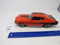 Left side view of the orange and black metal Chevrolet Chevelle model car with ruler for scale