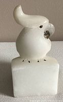 Front view of white alabaster bird sculpture on square base showing bird's face, crested feathers, and inlaid eyes.