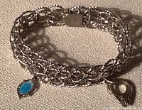 Silver charm bracelet coiled showing chain links and two charms, one blue oval, one wedding ring shape.