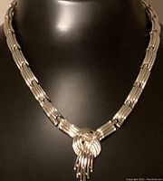 Front view of the Coro choker style silver necklace on a black display, showing the woven knot pendant and linked chain design.