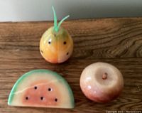 Front view of three alabaster stone fruit figurines: pineapple, apple, watermelon slice on wooden surface