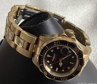 Front side view of the watch showing black dial with gold markers, hands, magnified date window, and black rotating bezel with gold numbers.