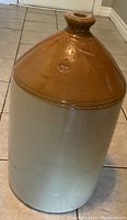 Full view of large two-toned stoneware jug showing brown glazed top and natural stone color bottom with spout neck.