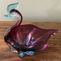 Side view of purple and blue Murano or Chalet glass bird dish showing elongated neck and flared wing-tail shape with smooth curves.