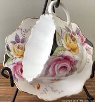 Side angled view of teacup inside matching saucer showing floral pattern and scalloped edges with gold trim