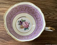 Top view of the teacup interior showing mauve and off-white colors, intricate gold trim, and central floral design