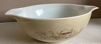 Side view of the large off-white Pyrex Cinderella bowl showing the brown Woodland design pattern around the exterior and the pouring spout.