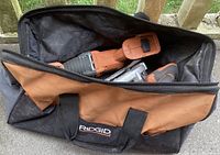 Ridgid branded tool bag holding the cordless power tools, partially open showing the tools inside.