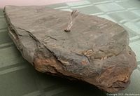 Side angle of the green flat rock showing the rough layered texture and braided wick inserted into a brass fitting.