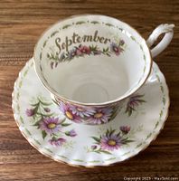 Top view of a Royal Albert teacup with purple Michaelmas Daisy flowers and gold 'September' inscription inside the cup. The saucer underneath has matching floral decoration.