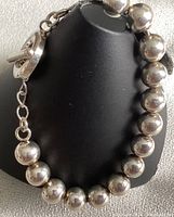 Close-up photo of polished sterling silver ball toggle bracelet displayed on a black stand. Shows round silver beads and circular toggle clasp.