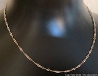 Photo of twisted silver chain necklace displayed on black mannequin bust, showing the full chain length and subtle shine.