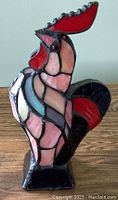 Front left side view showing vibrant stained glass rooster with red comb and tail, pink and blue body sections, mounted on black base.