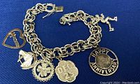 Full view of the silver charm bracelet showing all six charms and the safety clasp on a blue background.