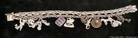 Full length photo of sterling silver charm bracelet with visible safety clasp and 10 varied charms including teddy bear, train engine, horse, and coin charm.