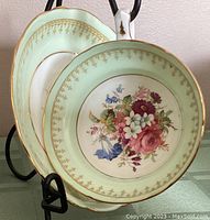 Front view of teacup and saucer showing mint green border, floral bouquet center, and gold trim