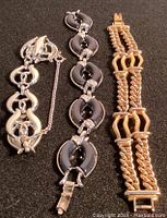 Photo showing three bracelets: gold-colored Monet chain bracelet and two Coro bracelets in grey and white/silver