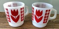 Side-by-side view of two Termocrisa milk glass mugs showing red tulip and red/white checkered patterns.