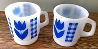 Two vintage milk glass mugs side by side showing blue tulip and checkered designs
