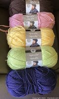 Five balls of yarn in dark brown, pink, yellow, light green, and dark blue colors arranged in a box.