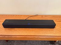 Front view of Sony HT-S200F sound bar on wooden table, blue LED indicator lit, power cable visible.