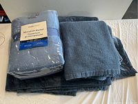 Lot showing two folded blue Microplush blankets and one folded blue mattress protector packed together.