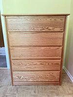 Front view of solid oak five-drawer dresser chest showing wood grain and full drawers.