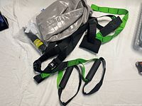 Photo shows deflated silver-gray GoodLife Fitness Swiss ball with black and green straps of the suspension trainer and black inflation pump on white sheet.