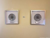 Photo showing both framed ceramic plate artworks mounted on wall, silver square frames and circular ceramic plates with radial designs.