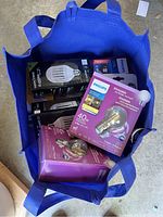 Blue tote full of assorted LED light bulb packages, mainly Philips brand, showing various sizes and shapes.