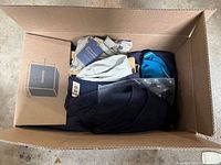 Box with mixed new men's pants, socks, shorts, and shirts inside, folded and packaged