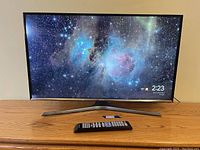 Front view of Samsung 32-inch UN32J5500AF Smart TV powered on showing image of space nebula with remote placed in front.