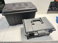 Large black and smaller gray Plano tool boxes side by side on white surface