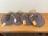 Four dark brown Sloggers men’s classic cotton hats arranged in a row on wooden surface, showing tags and wide brims.