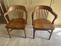 Two solid oak arm chairs placed side by side showing front and side views revealing design and finish.