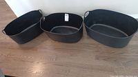 Three black plastic bins of different sizes arranged on wooden floor, all with handles.