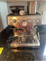 Full front view of espresso machine on countertop with hopper, analog gauge, steam wand and accessories on drip tray