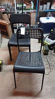 Four black plastic chairs with perforated seats and backs in a storage area.