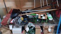 Photo showing brooms, gloves, keyboard, mouse, plunger, scrub brush, and cleaning spray on metal rack