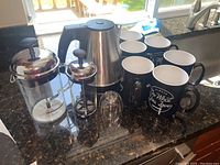 Full lot showing six black WEWORK ceramic coffee cups, large and small French presses, stainless steel electric kettle, and glass cold brew coffee maker.