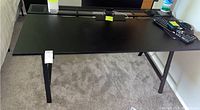 Full view of black computer desk with items on top, showing legs and tabletop surface.