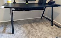 Front view of black computer desk showing the smooth surface and adjustable metal legs.