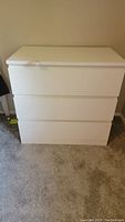 Full view of white dresser showing three drawers and overall shape on carpeted floor.