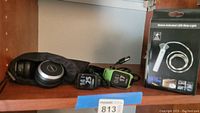 Jabra wired headphones with Logitech branded pouch on wooden shelf next to two TomTom smart watches and boxed motion activated LED strip light.