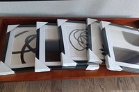 Five framed abstract art prints laid on wooden tray, framed in black with white matting and protective white corner covers.