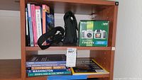 Shelf showing the boxed Fujifilm FinePix 3800 digital camera, black camera bag, and books about the Pacific Northwest.