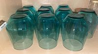 Nine blue glass tumblers upside down on a shelf, showing their medium blue color and faceted shape.