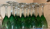 Side view of twelve green cut glass stemware showing diamond crosshatch pattern on bowls and clear glass stems and bases.