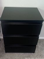 Front view of dark colored nightstand showing the three drawers and flat top surface.